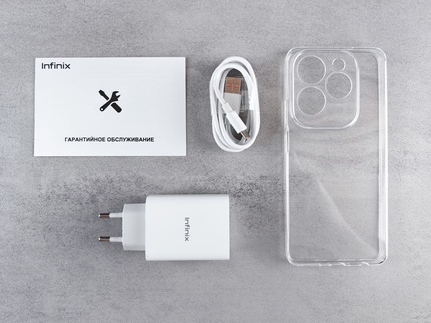 A flat lay arrangement of smartphone accessories and electronic devices including a white Infinix-branded charging brick with two prongs, a white USB-C charging cable coiled neatly with a USB-A connec